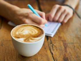 Notizen schreibende Person mit Kaffee